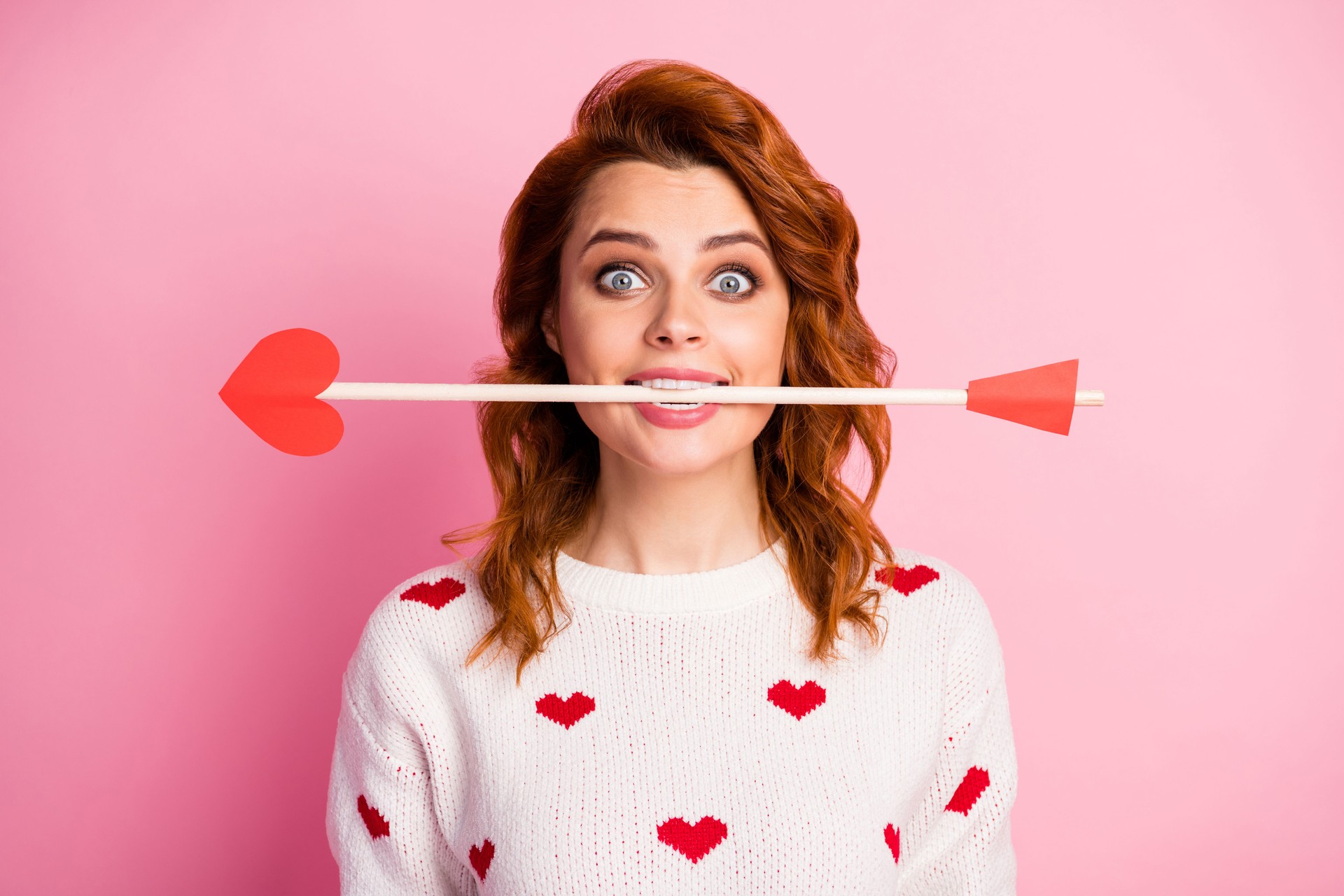 Close-up portrait of her she nice attractive lovely pretty cute amorous cheerful cheery funky childish wavy-haired girl angel holding in teeth arrow date isolated on pink pastel color background